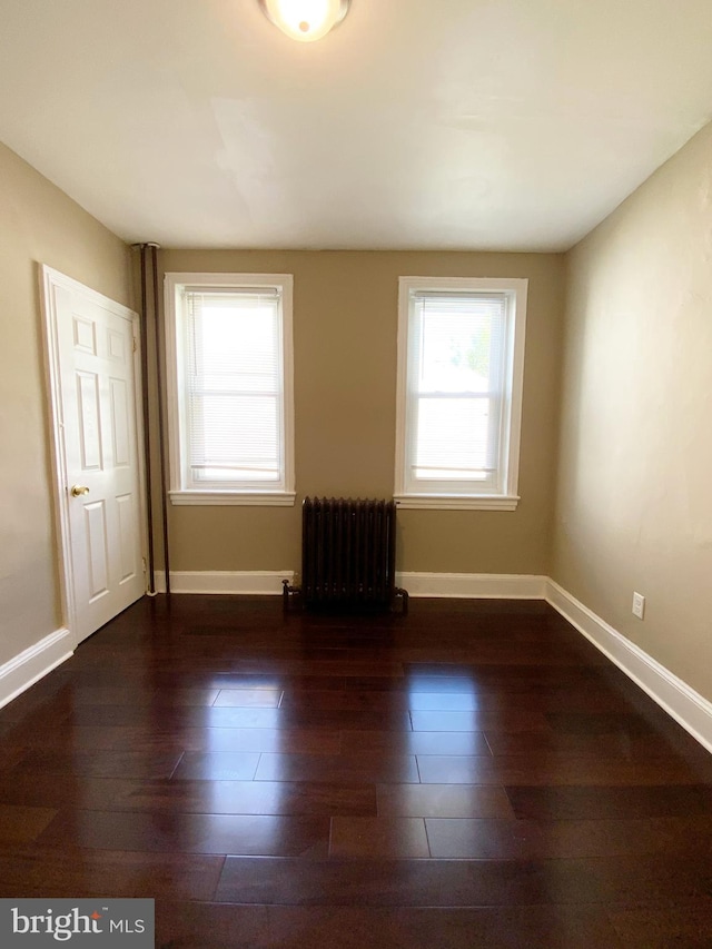 empty room featuring baseboards, wood finished floors, and radiator