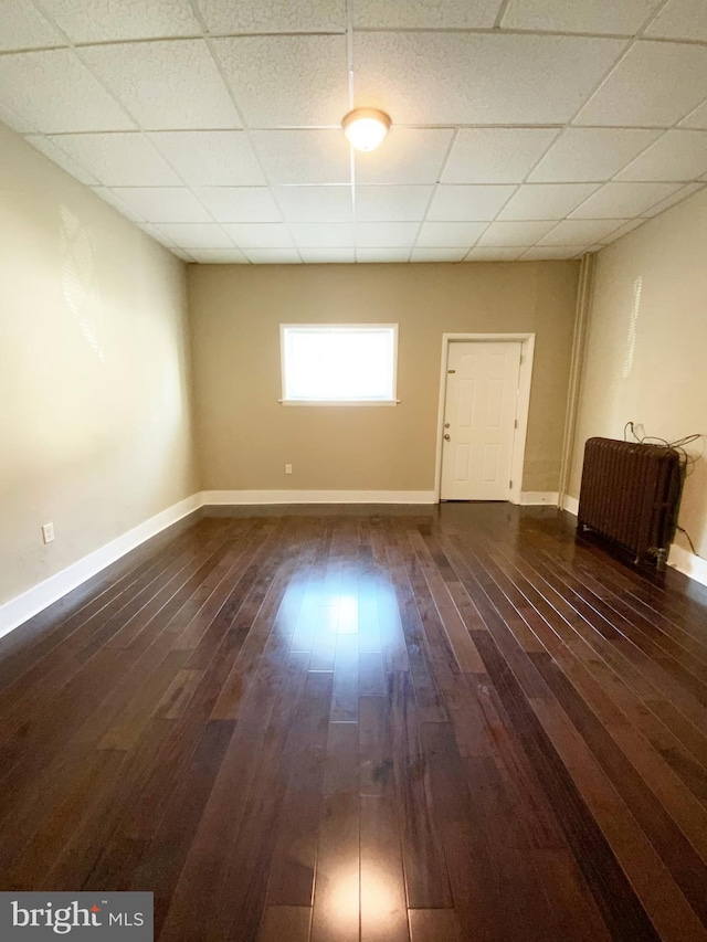 empty room featuring dark wood-style flooring, baseboards, and a paneled ceiling