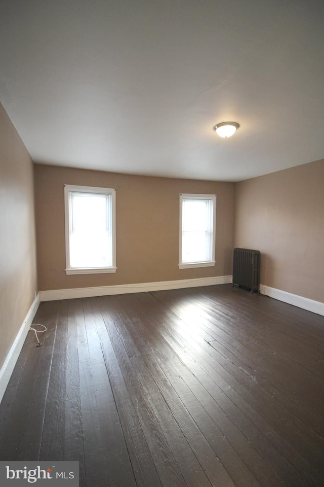 unfurnished room with baseboards, dark wood-style flooring, and radiator