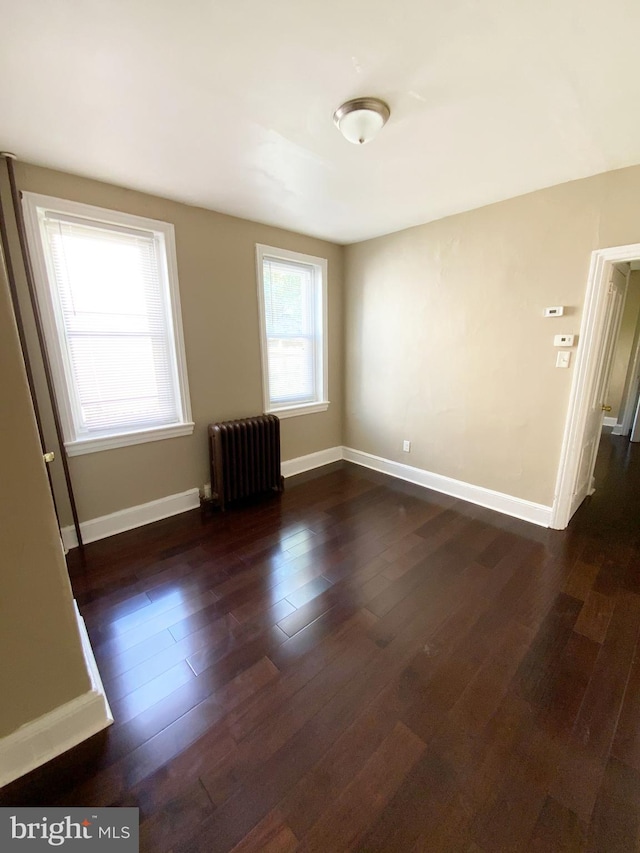 empty room with dark wood-type flooring, baseboards, and radiator heating unit
