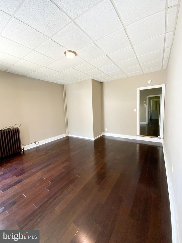 unfurnished room with baseboards, dark wood-style floors, and radiator heating unit