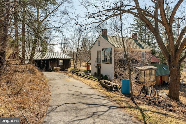 view of front of property with a standing seam roof, a chimney, metal roof, aphalt driveway, and stucco siding