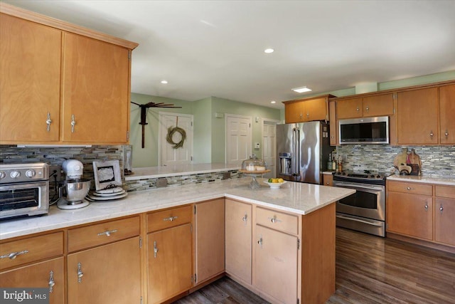 kitchen featuring decorative backsplash, appliances with stainless steel finishes, a toaster, a peninsula, and dark wood-type flooring