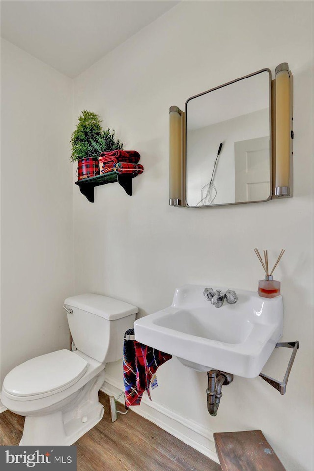 half bath featuring toilet, baseboards, a sink, and wood finished floors