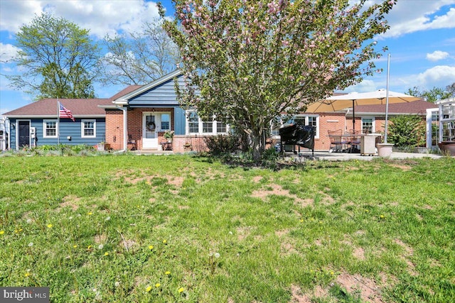 rear view of house with brick siding, a lawn, and a patio area