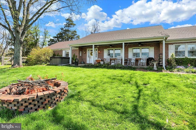 view of front of property with a hot tub, an outdoor fire pit, brick siding, ceiling fan, and a front yard