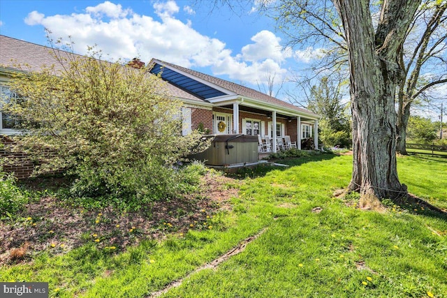 exterior space featuring a hot tub, brick siding, and a yard