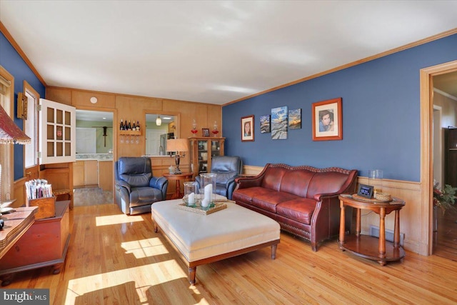 living room with crown molding, wood walls, wainscoting, and wood finished floors