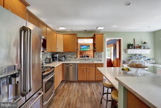 kitchen with brown cabinets, tasteful backsplash, a sink, light wood finished floors, and stainless steel appliances