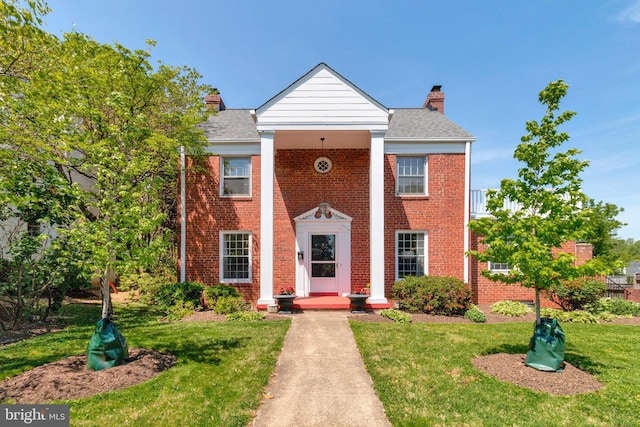greek revival house featuring a chimney, brick siding, and a front yard