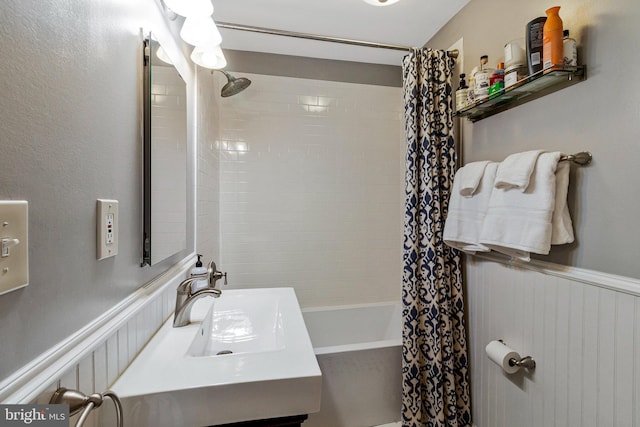 full bathroom with shower / bath combination with curtain, a sink, and a wainscoted wall