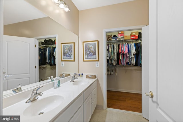 bathroom featuring a sink, double vanity, a spacious closet, and baseboards