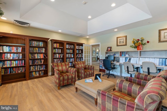 interior space with wood finished floors, bookshelves, visible vents, recessed lighting, and a raised ceiling