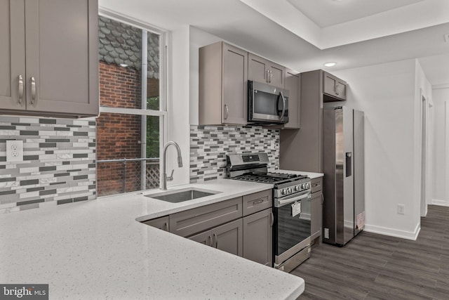 kitchen with a sink, stainless steel appliances, gray cabinets, backsplash, and baseboards