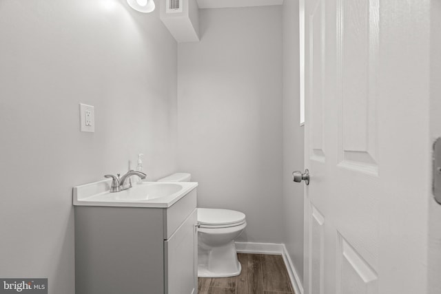half bath featuring toilet, wood finished floors, visible vents, baseboards, and vanity
