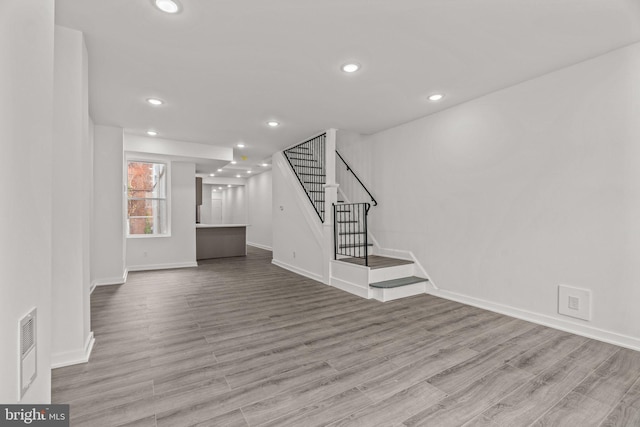 unfurnished living room with baseboards, stairway, recessed lighting, and wood finished floors