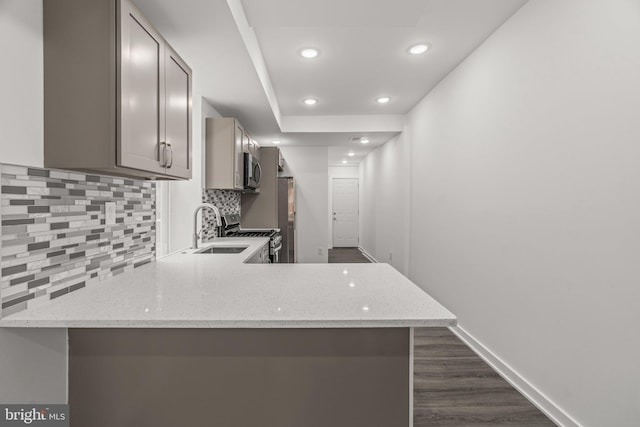 kitchen featuring a sink, gray cabinets, decorative backsplash, appliances with stainless steel finishes, and dark wood-style floors