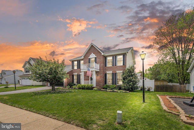 view of front facade featuring fence, brick siding, a balcony, a lawn, and driveway