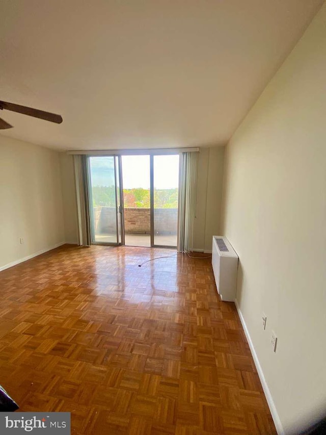 empty room with ceiling fan, floor to ceiling windows, radiator heating unit, and baseboards