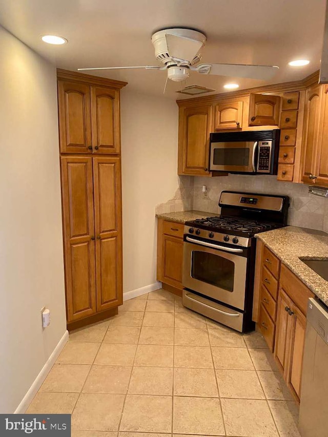 kitchen with light stone countertops, stainless steel appliances, brown cabinetry, and backsplash