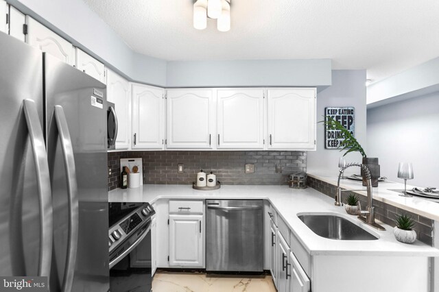 kitchen with appliances with stainless steel finishes, a sink, light countertops, marble finish floor, and white cabinetry