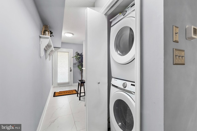 laundry area with baseboards, stacked washer and clothes dryer, marble finish floor, and laundry area