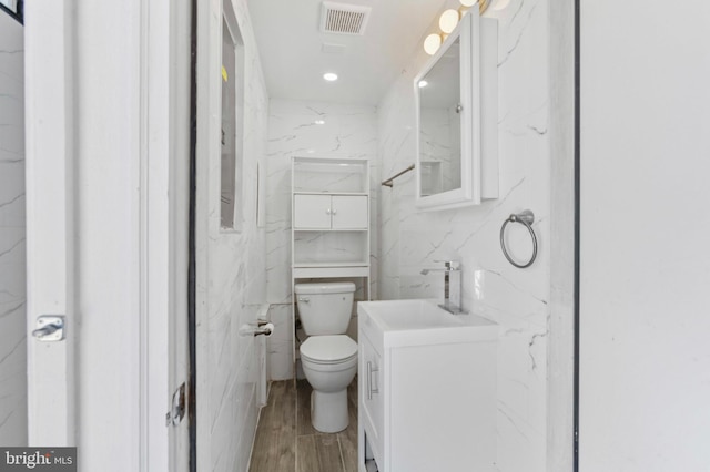 bathroom with vanity, toilet, tile walls, wood finished floors, and visible vents