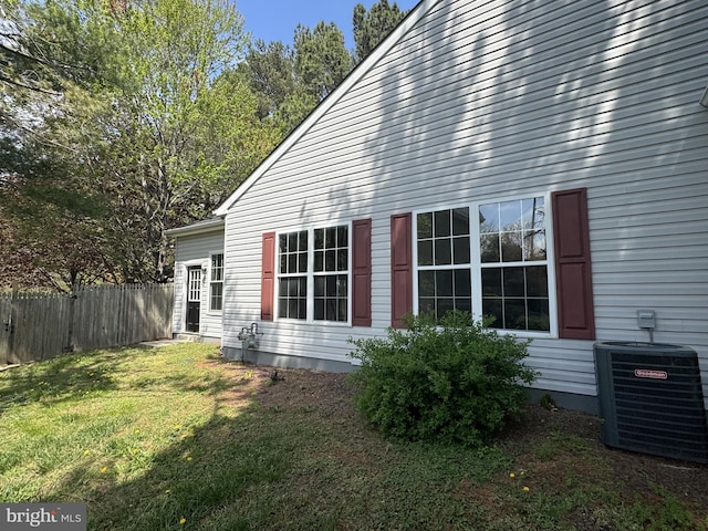 view of side of property featuring a lawn, central AC unit, and fence
