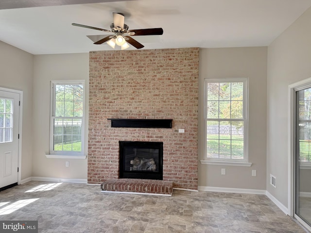 unfurnished living room featuring a healthy amount of sunlight, a ceiling fan, and stone finish flooring