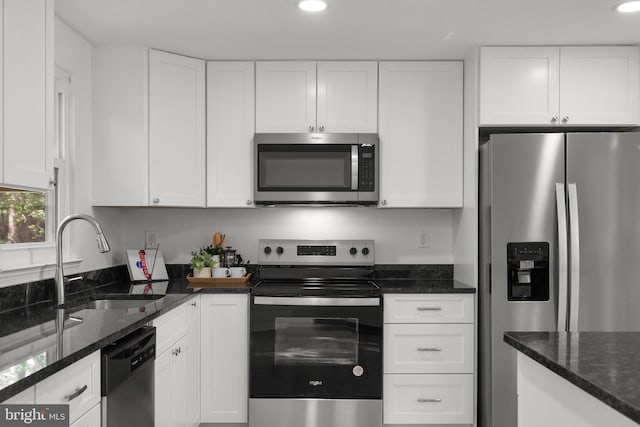 kitchen featuring white cabinets, appliances with stainless steel finishes, a sink, and dark stone counters