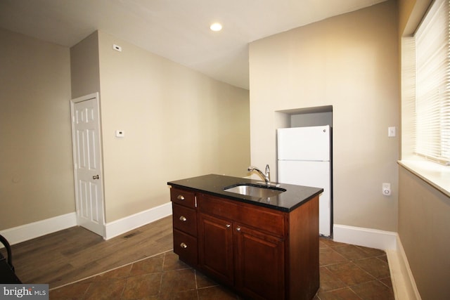 kitchen featuring an island with sink, a sink, freestanding refrigerator, baseboards, and recessed lighting