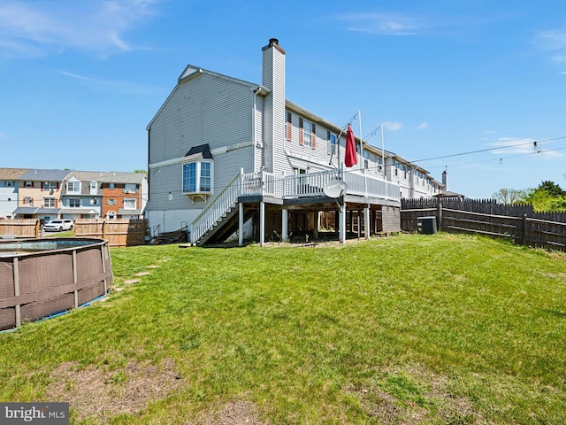 rear view of house featuring a chimney, a wooden deck, stairway, a fenced backyard, and a yard