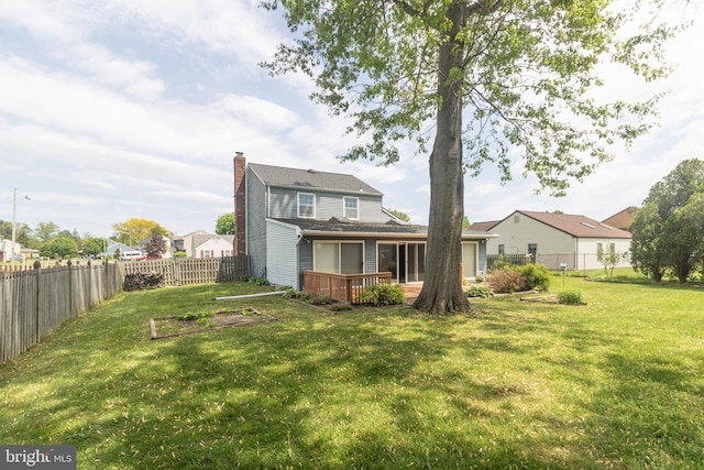 back of house featuring a lawn, a chimney, a fenced backyard, and a wooden deck