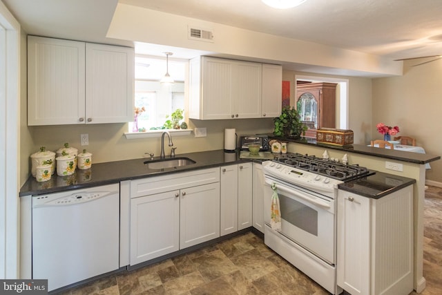 kitchen with dark countertops, a sink, white appliances, a peninsula, and visible vents