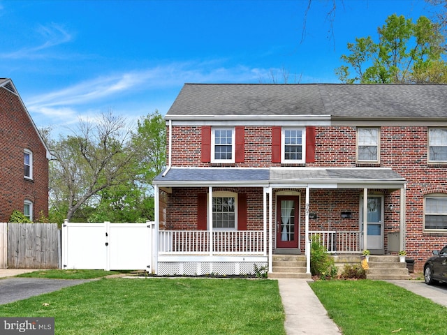 view of front of home with brick siding, fence, a gate, and a front lawn