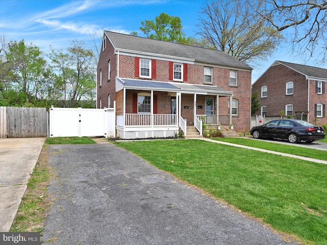 view of front facade with a porch, a gate, brick siding, fence, and a front lawn