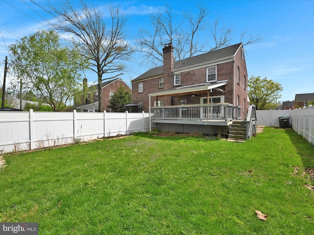 back of house featuring brick siding, a deck, a fenced backyard, a chimney, and a lawn