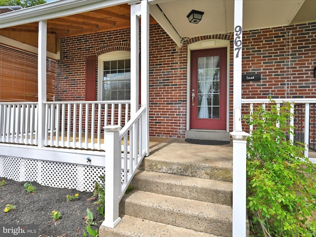 view of exterior entry featuring a porch and brick siding