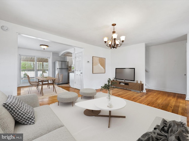 living room featuring baseboards, arched walkways, light wood-style flooring, and a notable chandelier