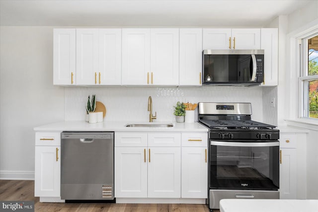 kitchen with appliances with stainless steel finishes, tasteful backsplash, a sink, light countertops, and white cabinets