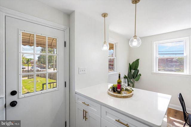 kitchen with wood finished floors, baseboards, light countertops, white cabinets, and decorative light fixtures
