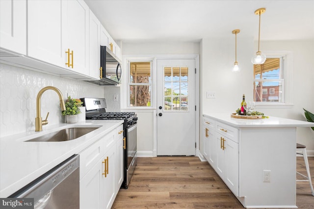 kitchen with a peninsula, a kitchen bar, white cabinetry, a sink, and appliances with stainless steel finishes