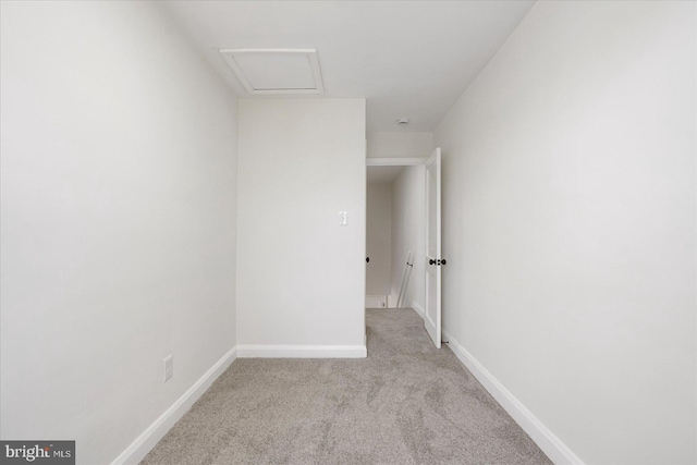 carpeted empty room featuring baseboards and attic access