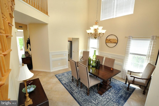 dining area with wainscoting, a towering ceiling, a decorative wall, light tile patterned floors, and a notable chandelier