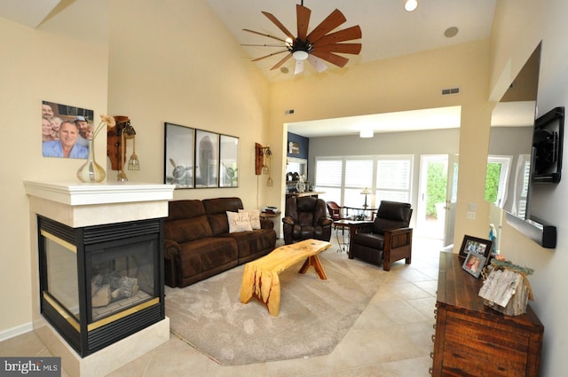 living area featuring a multi sided fireplace, a ceiling fan, visible vents, tile patterned flooring, and high vaulted ceiling
