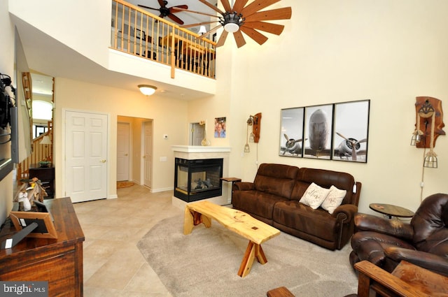 living area with ceiling fan, tile patterned flooring, a multi sided fireplace, baseboards, and a towering ceiling