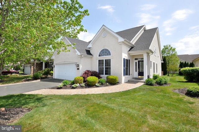 view of front of house with driveway, a front lawn, an attached garage, a shingled roof, and stucco siding