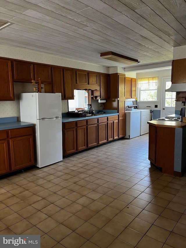 kitchen with freestanding refrigerator, light tile patterned flooring, brown cabinets, wooden ceiling, and washing machine and clothes dryer