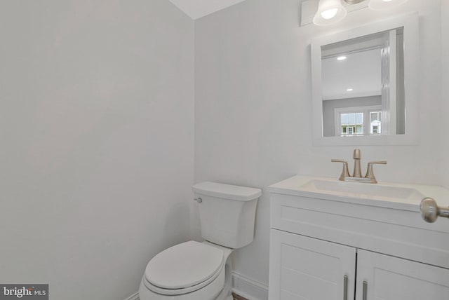 half bathroom featuring toilet, baseboards, and vanity
