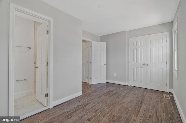 unfurnished bedroom featuring visible vents, wood finished floors, baseboards, a closet, and ensuite bathroom